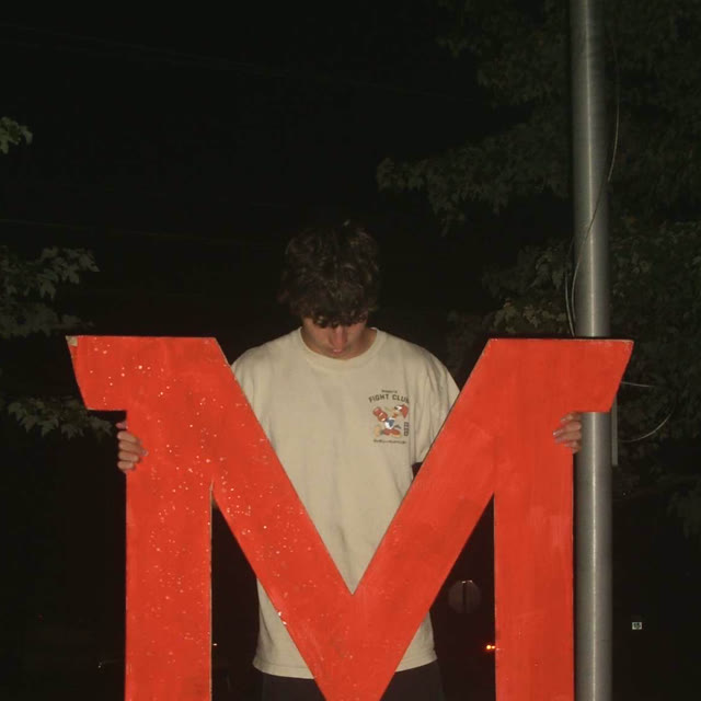 Jack Hiebel holding a big red letter M at night